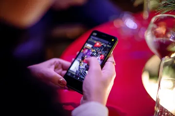 A cheerful woman in traditional clothing using her smartphone during a festive moment, showing how easily the KKBDT app fits into everyday life.