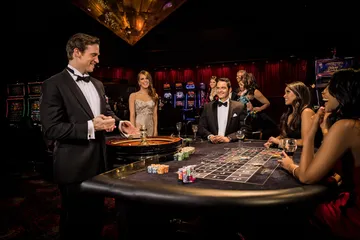A professional dealer in a tuxedo greeting players at the roulette table, symbolizing the authentic live casino feel at KKBDT.